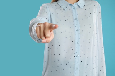 Photo of Woman pointing at something on light blue background, closeup. Finger gesture