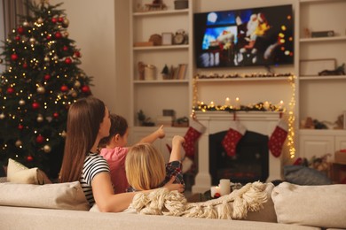 Photo of Mother with her children watching TV in cosy room. Christmas atmosphere