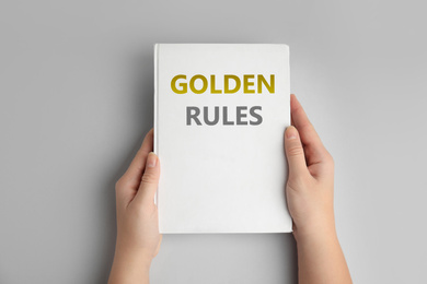 Woman holding book with phrase GOLDEN RULES on grey background, top view