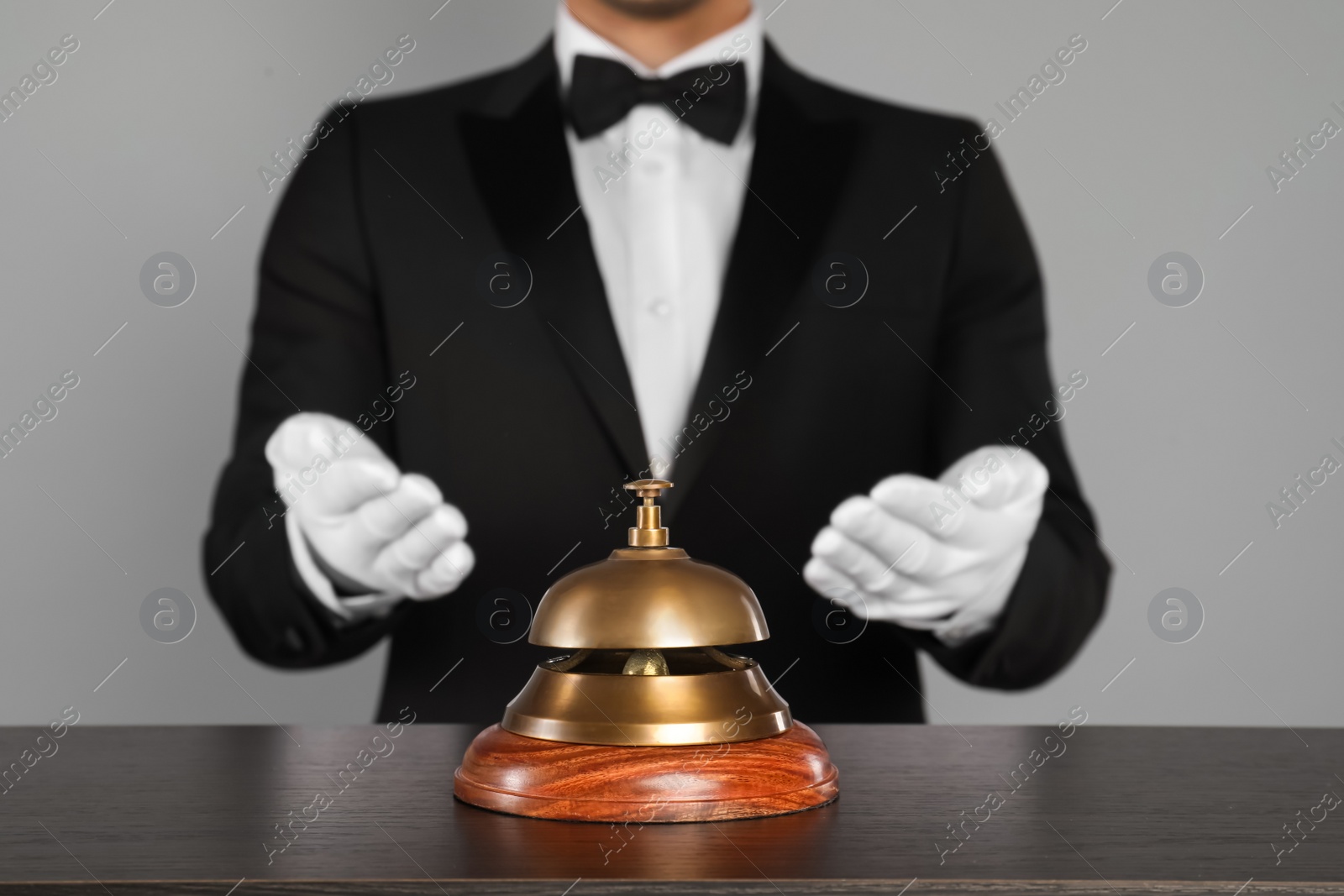 Photo of Butler at desk with service bell on grey background, closeup