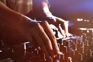 Photo of DJ creating music on modern console mixer in night club, closeup