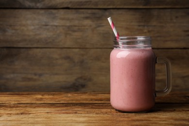 Photo of Mason jar with delicious berry smoothie on wooden table. Space for text