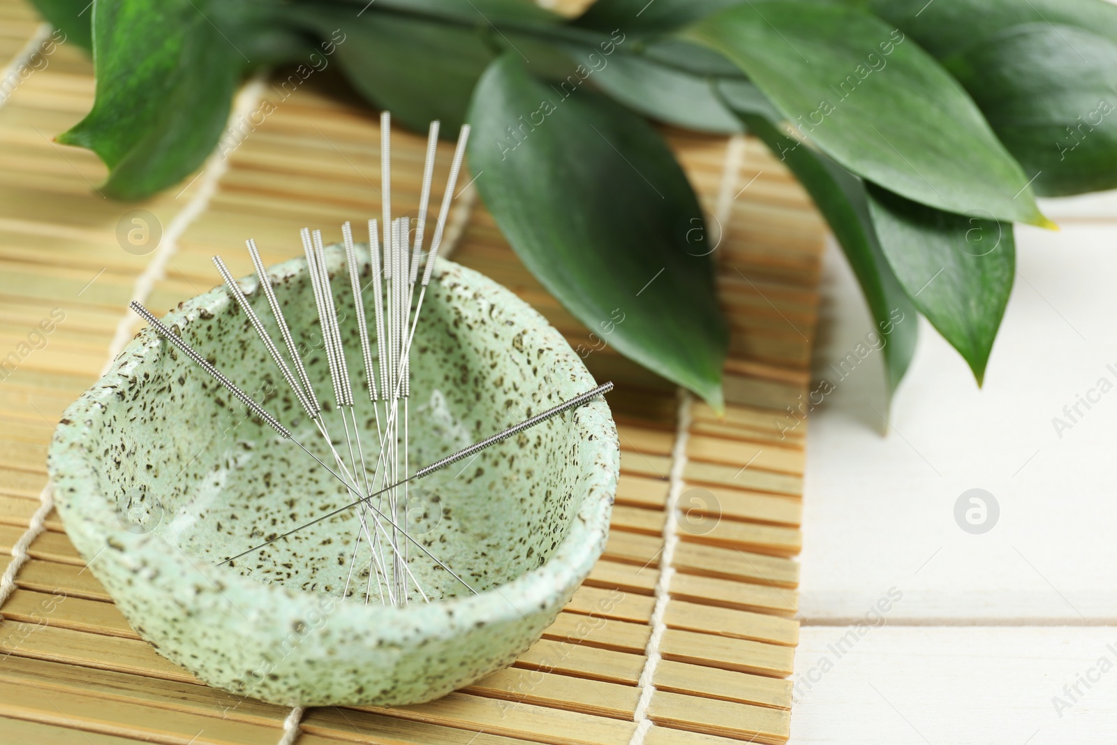 Photo of Bowl with acupuncture needles on white wooden table, closeup. Space for text