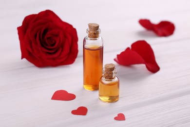 Bottles of love potion, paper hearts and red rose flower on white wooden table