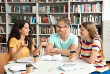 Photo of Young people discussing group project at table in library