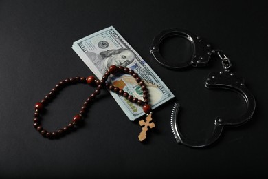 Photo of Dollars, handcuffs and prayer beads on black table