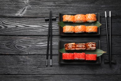 Photo of Different sushi rolls and chopsticks on black wooden table, flat lay. Space for text