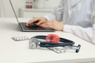 Photo of Endocrinologist working at table, focus on stethoscope and model of thyroid gland