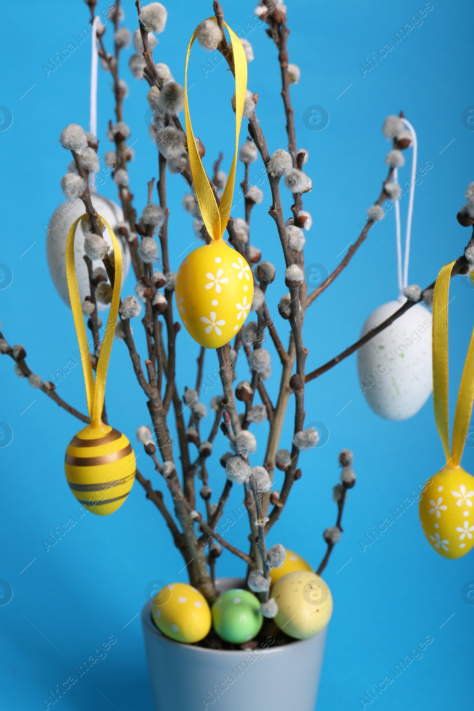 Photo of Beautiful willow branches with painted eggs in pot on light blue background. Easter decor