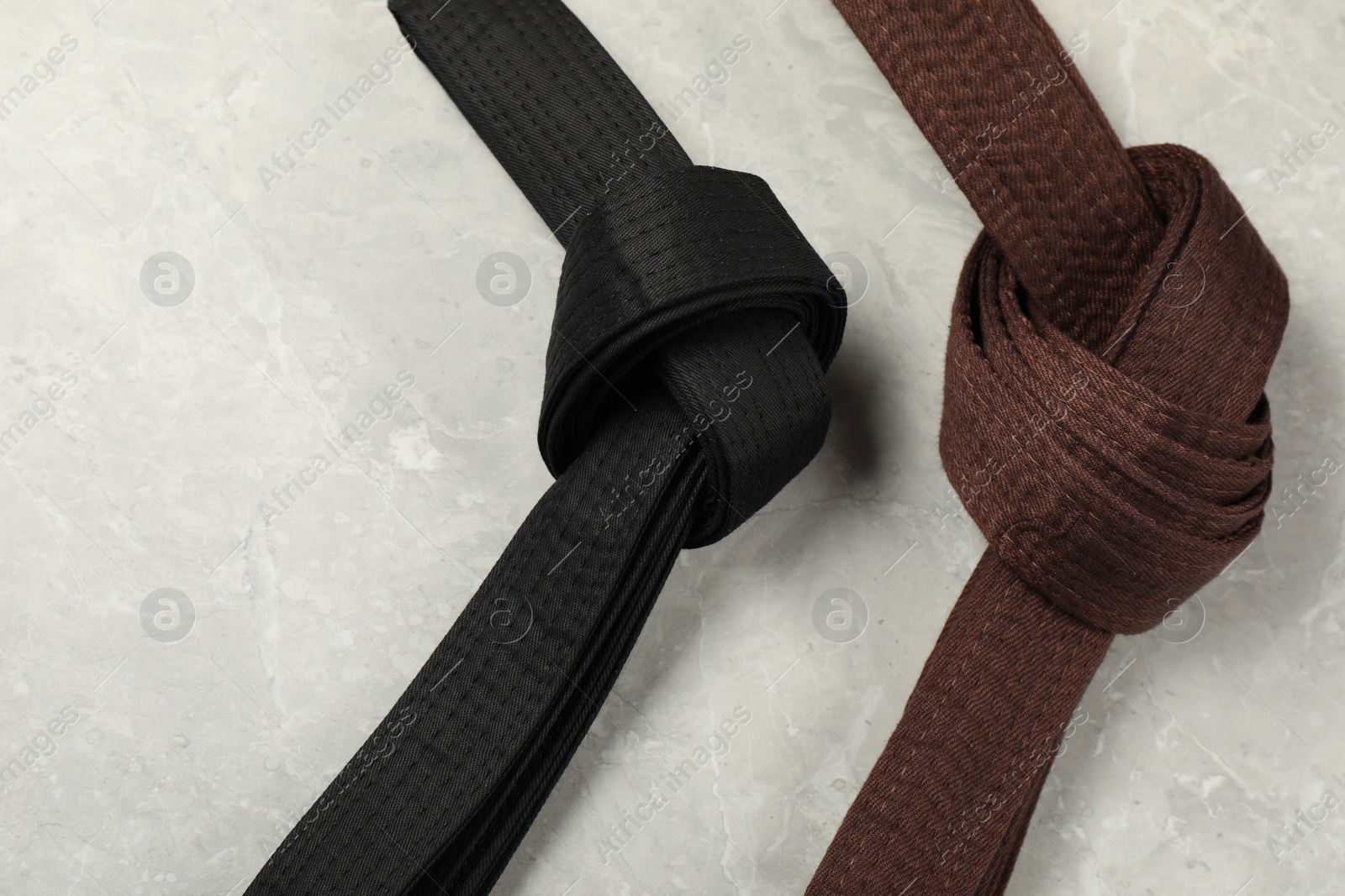 Photo of Black and brown karate belts on gray marble background, flat lay. Space for text