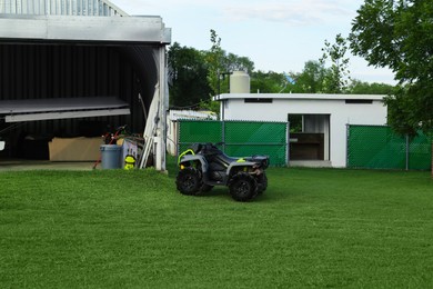 Photo of Modern quad bike on green grass and white airplane in big hangar outdoors