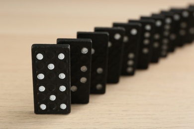 Photo of Black domino tiles with white pips on wooden table, closeup