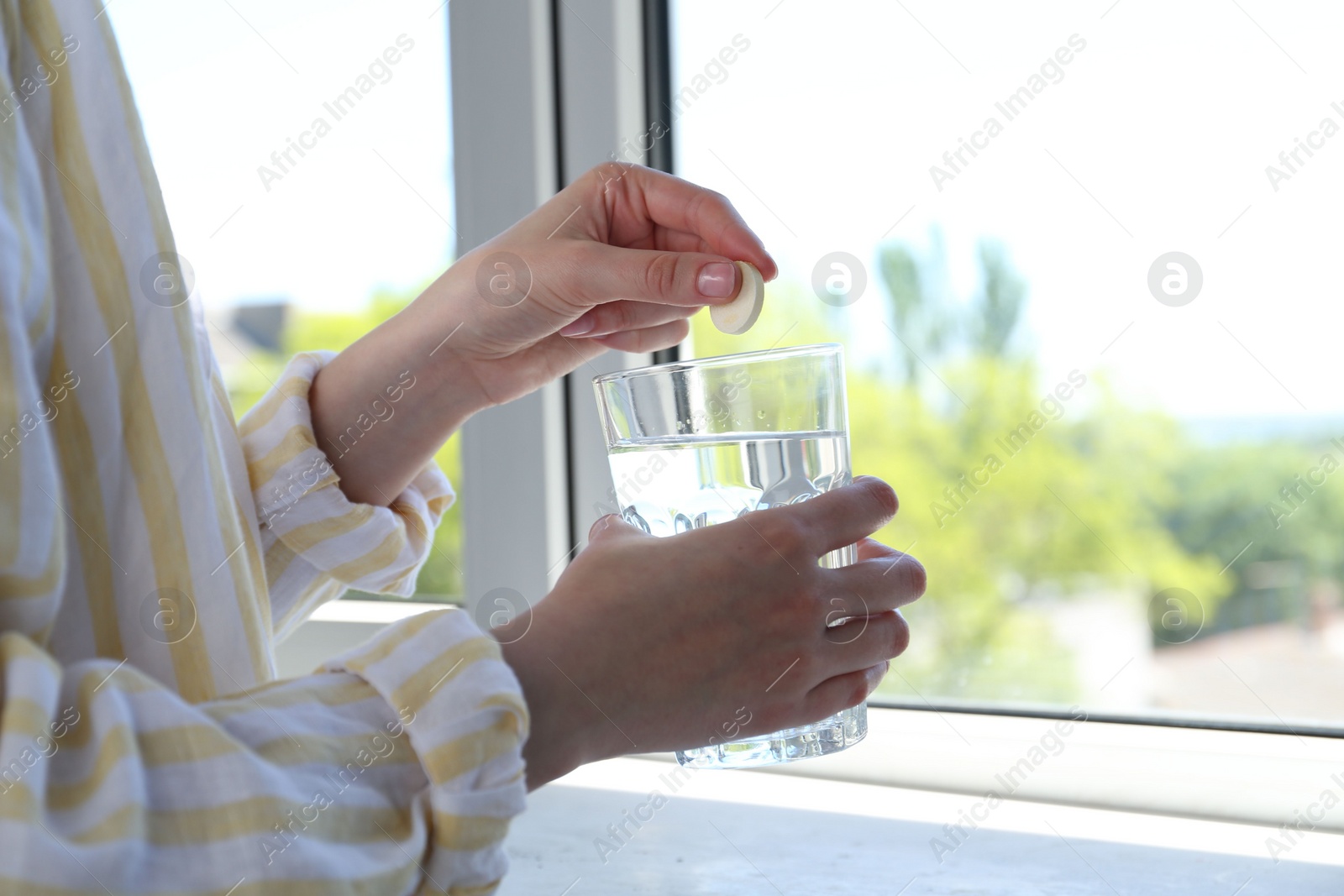 Photo of Woman putting effervescent pill into glass of water indoors, closeup