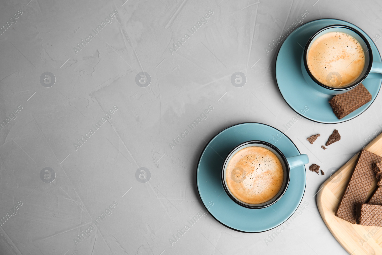 Photo of Breakfast with delicious wafers and cups of coffee on grey table, flat lay. Space for text