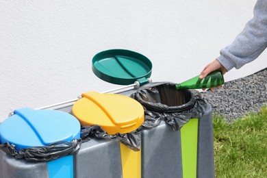 Woman throwing glass bottle in bin outdoors, closeup. Recycling concept