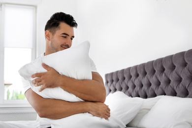 Photo of Young man with soft pillow on bed at home