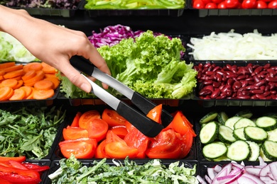 Young woman taking fresh tomatoes from salad bar, closeup