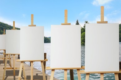 Image of Wooden easels with blank canvases near river on sunny day 