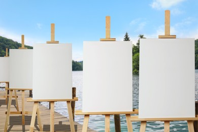 Wooden easels with blank canvases near river on sunny day 