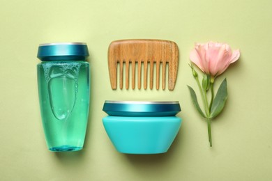 Hair care cosmetic products, wooden comb and flower on light green background, flat lay