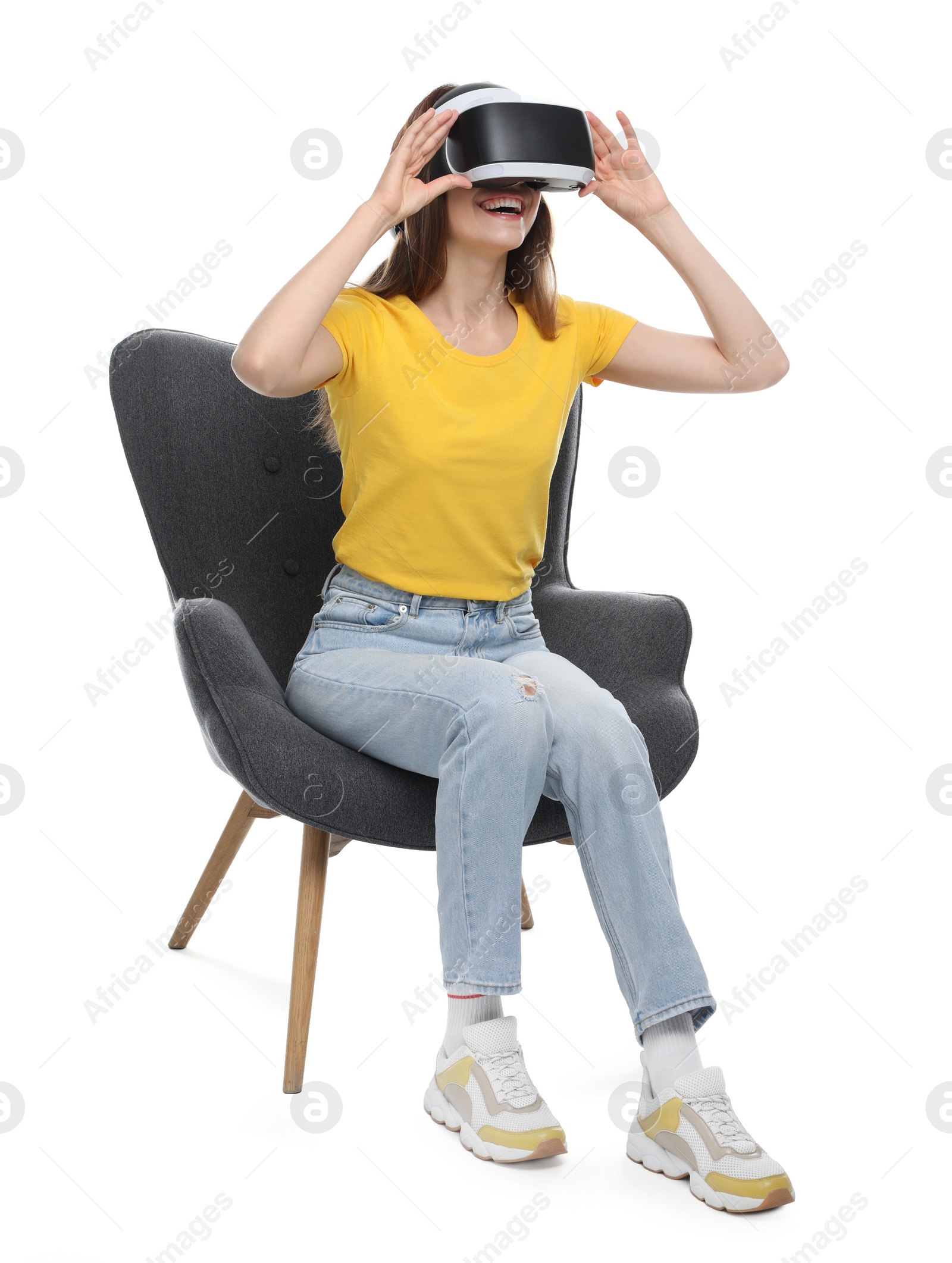 Photo of Smiling woman using virtual reality headset while sitting in armchair against white background