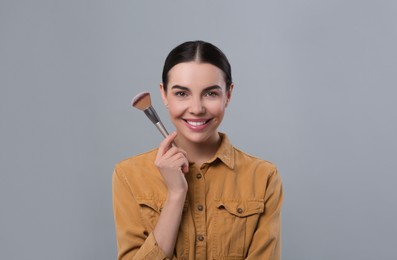 Photo of Happy woman with makeup brush on light grey background, space for text