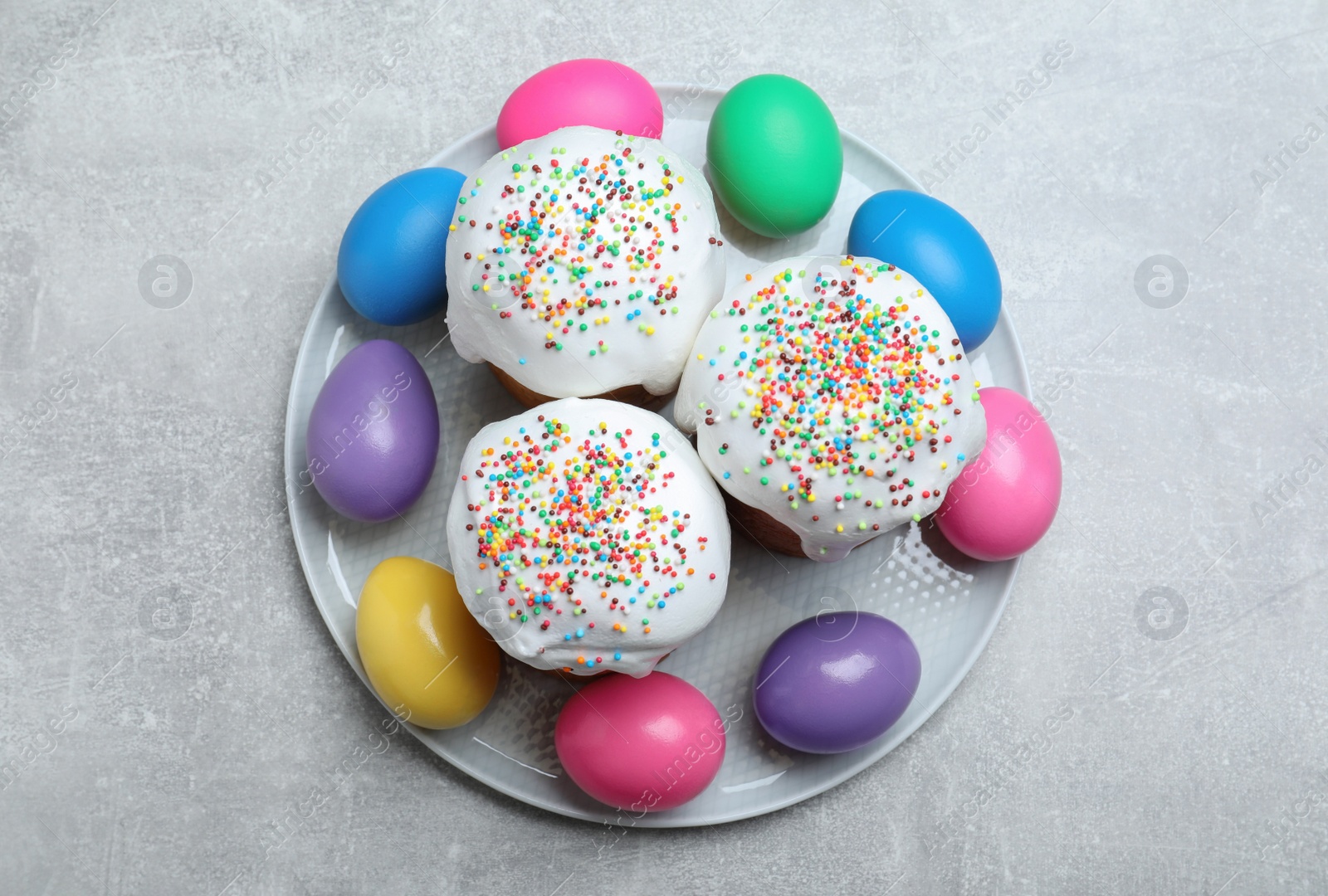 Photo of Easter cakes and colorful eggs on light grey table, top view