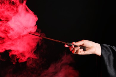 Photo of Magician holding wand in smoke on dark background, closeup