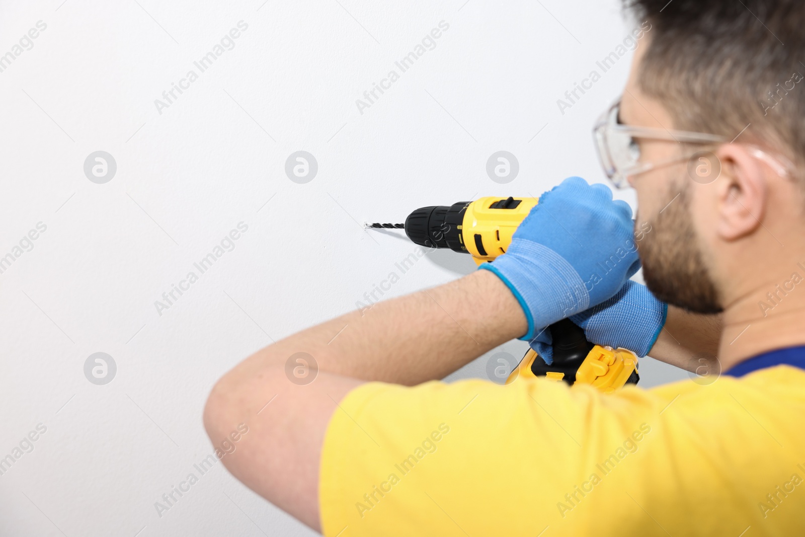 Photo of Young worker using electric drill indoors. Space for text