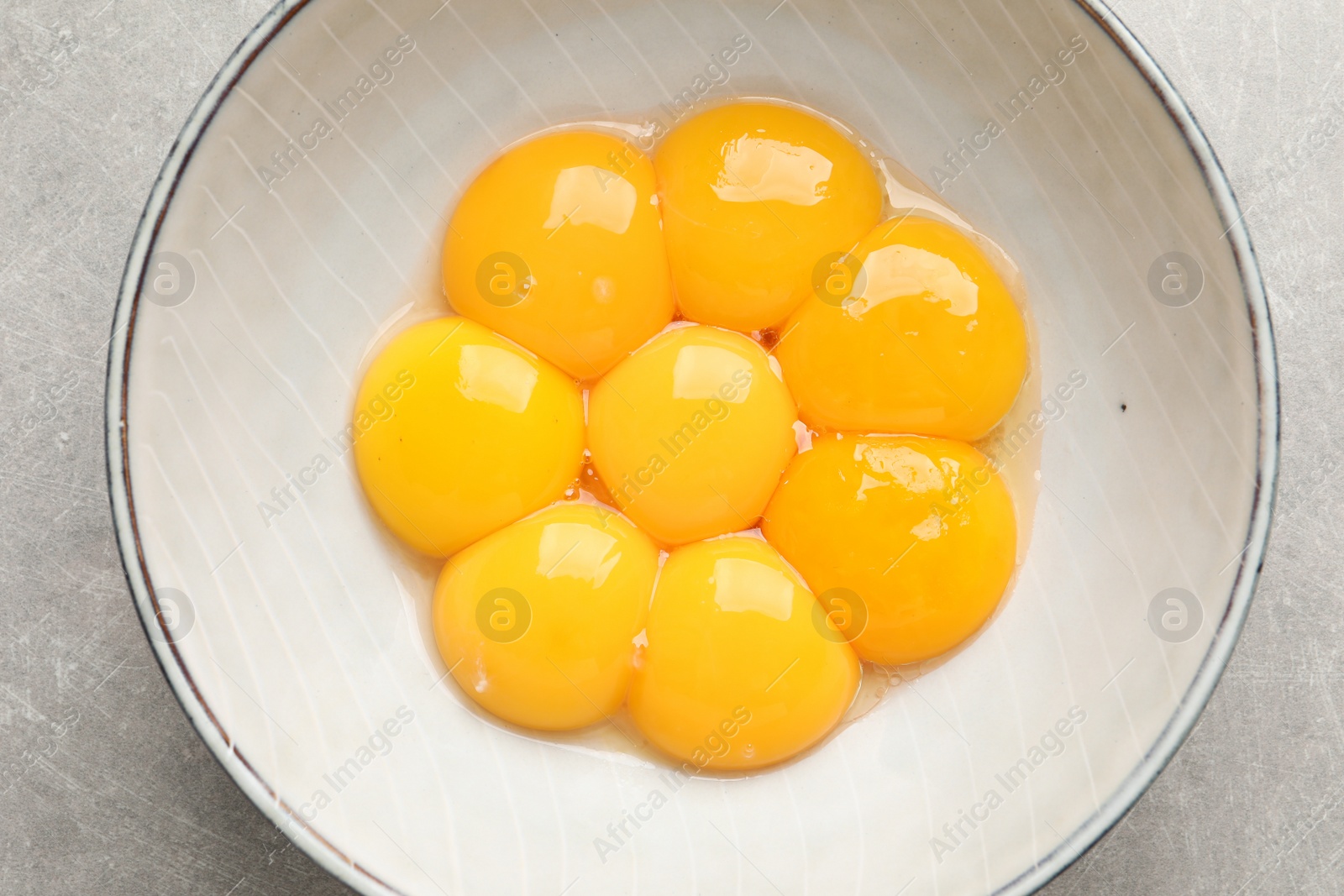 Photo of Bowl with raw egg yolks on grey table, top view