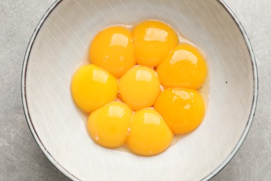 Photo of Bowl with raw egg yolks on grey table, top view