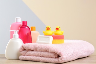 Photo of Baby cosmetic products, toys and towel on table against color background