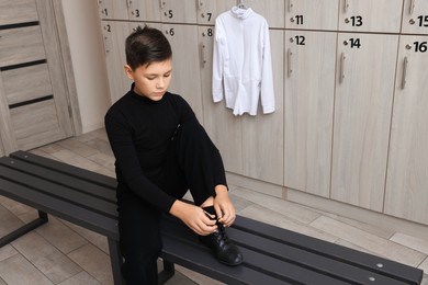 Photo of Little boy putting on shoes in locker room