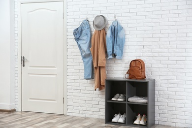 Stylish hallway interior with door, shoe rack and clothes hanging on brick wall