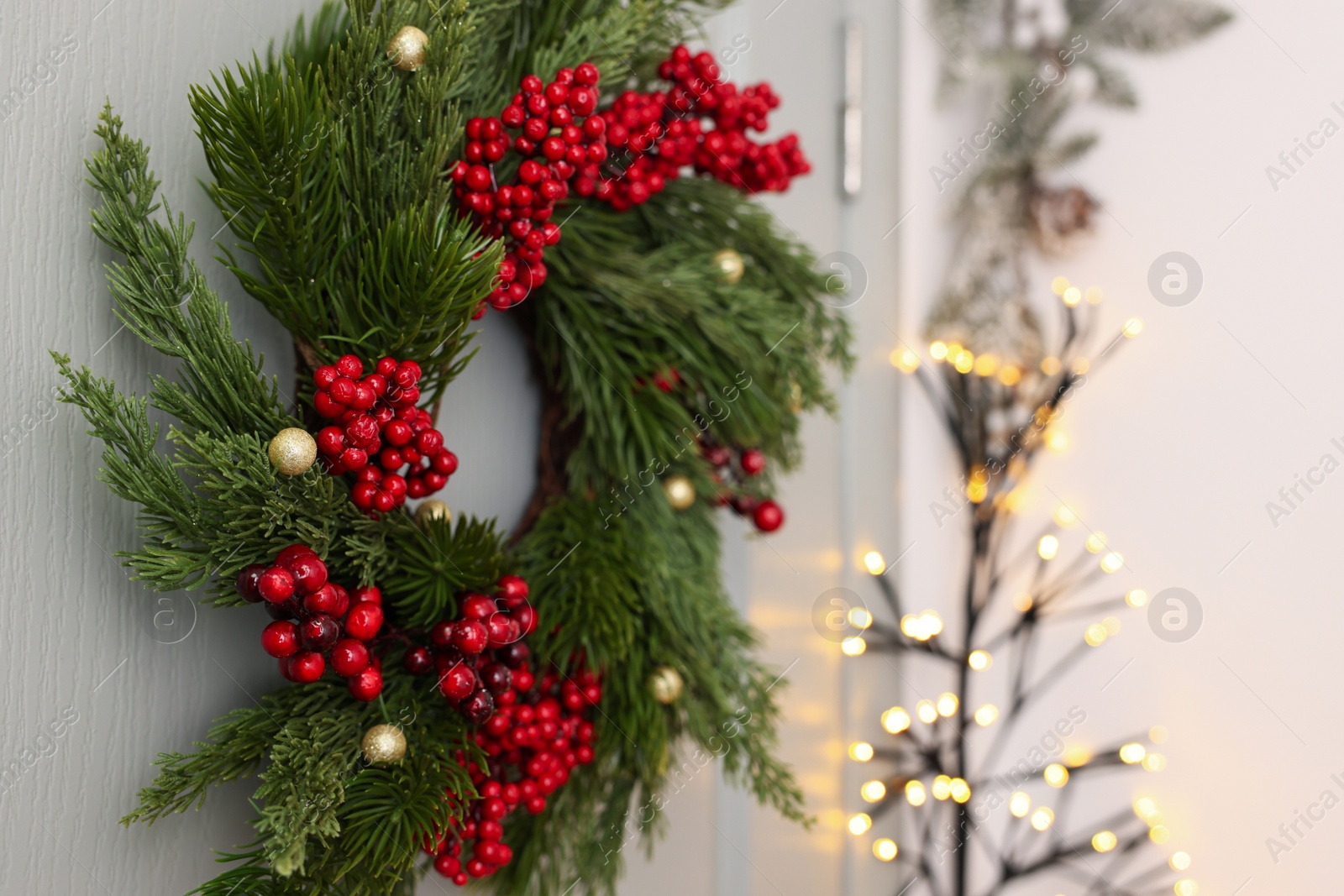 Photo of Beautiful Christmas wreath with red berries and decor hanging on white door, closeup. Space for text