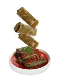 Image of Delicious stuffed grape leaves falling into plate on white background 
