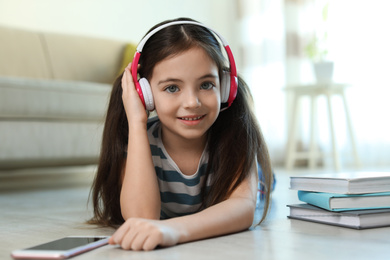 Photo of Cute little girl with headphones and smartphone listening to audiobook at home