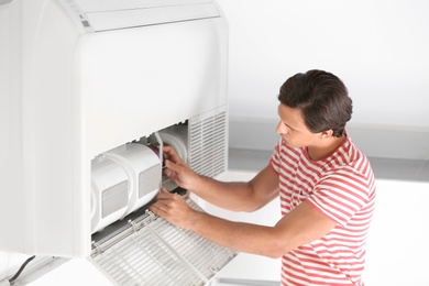 Young man fixing air conditioner at home