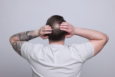 Photo of Baldness concept. Man with bald spot on light grey background, back view