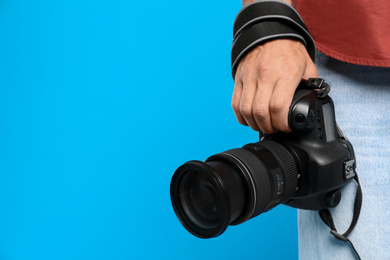 Photo of Professional photographer with modern camera on light blue background in studio, closeup. Space for text