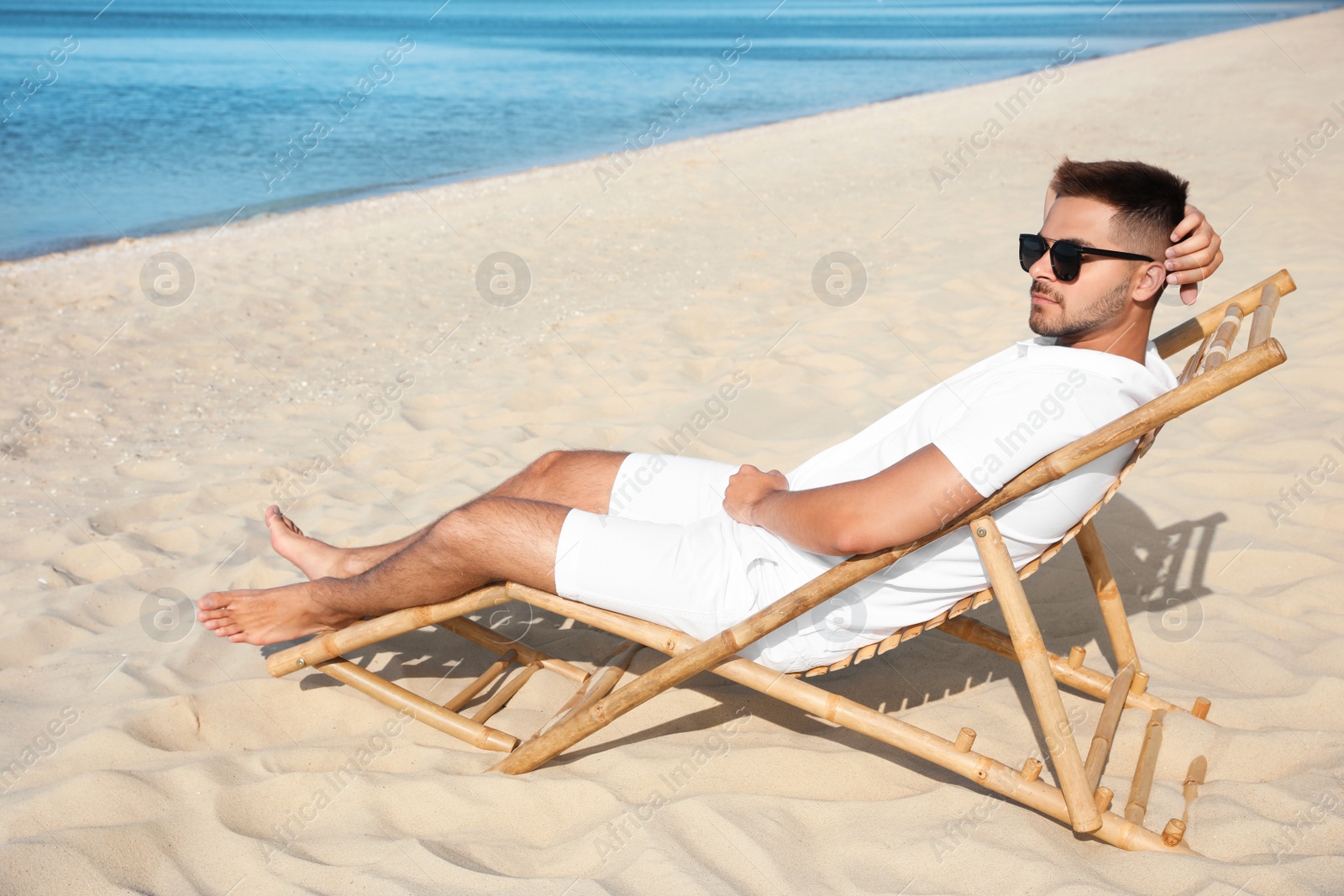 Photo of Young man relaxing in deck chair on sandy beach