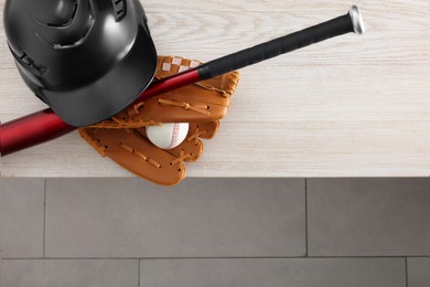 Photo of Baseball bat, batting helmet, leather glove and ball on wooden bench indoors, above view. Space for text