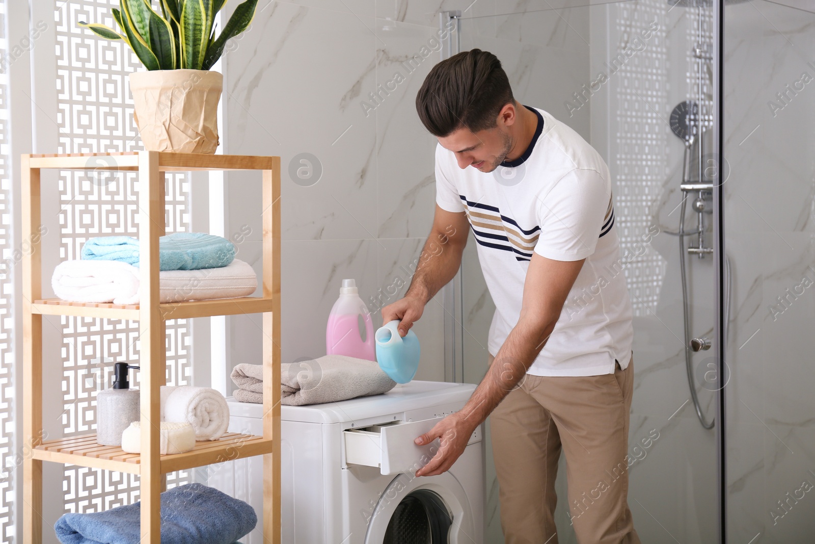 Photo of Man pouring detergent into washing machine drawer in bathroom. Laundry day