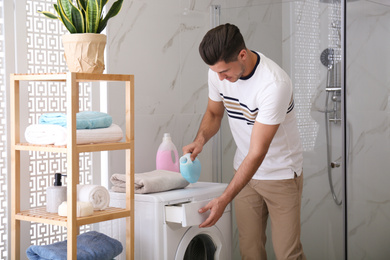 Photo of Man pouring detergent into washing machine drawer in bathroom. Laundry day