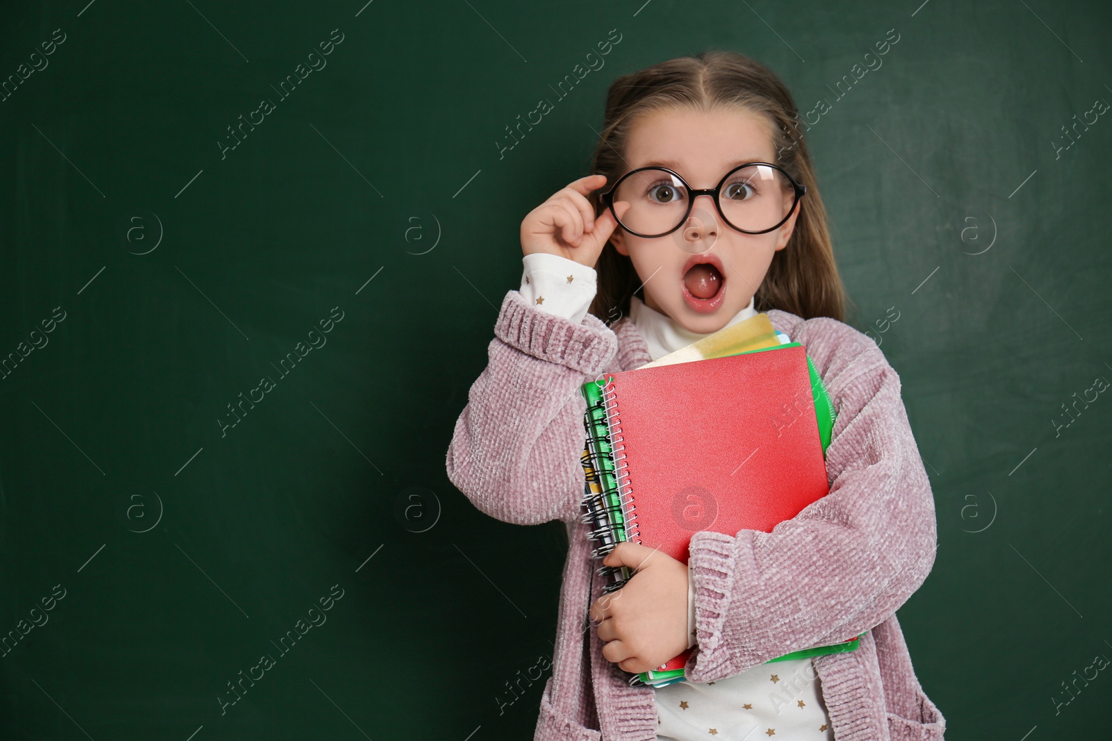 Photo of Cute little child wearing glasses near chalkboard, space for text. First time at school