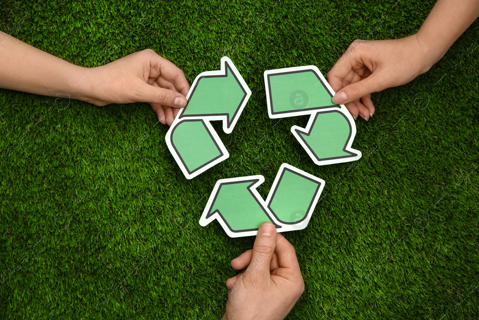 Photo of People holding paper recycling symbol above green grass, top view