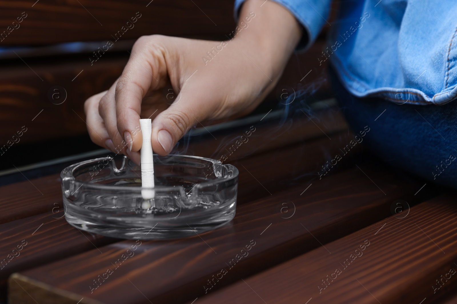 Photo of Woman putting out cigarette in ashtray on wooden bench, closeup