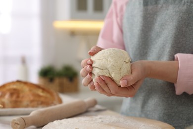 Photo of Making bread. Woman holding dough at table in kitchen, closeup
