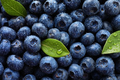 Photo of Wet fresh blueberries with green leaves as background, top view