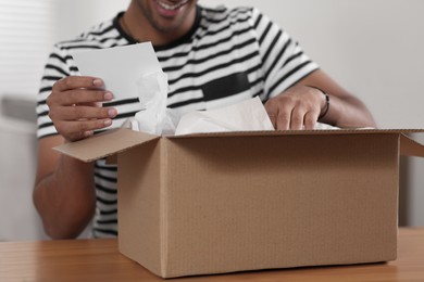 Young man holding greeting card near parcel with Christmas gift, closeup